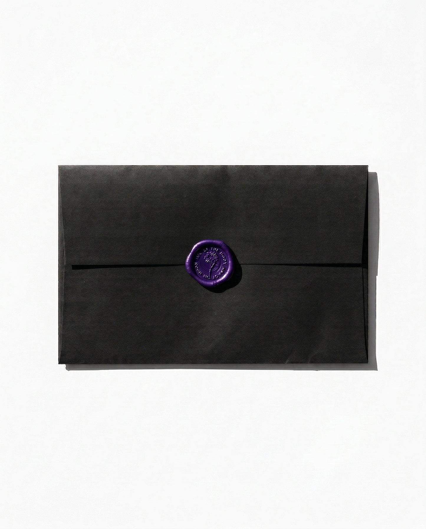 Black paper envelope with a dark purple wax seal against a white backdrop.