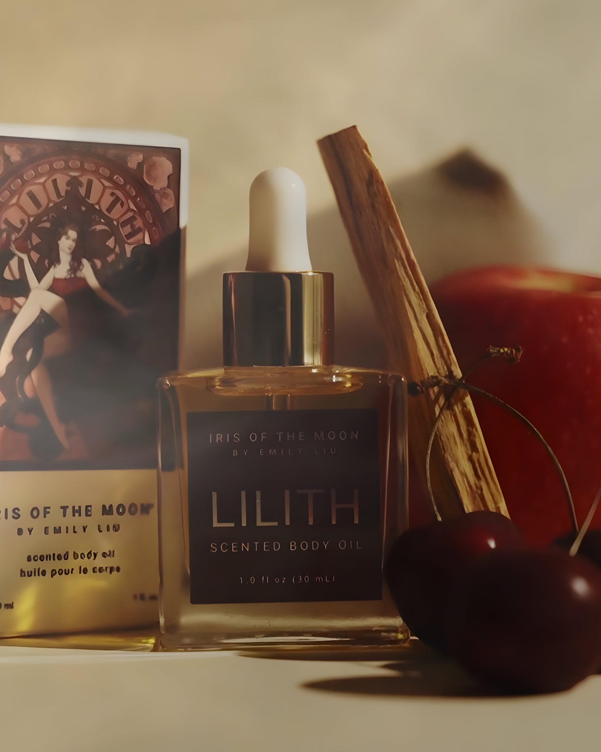 Lilith scented body oil with a palo santo stick, cherries, and an apple on a neutral background