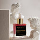 Persephone scented body oil bottle with gold cap on a pedestal in front of classical sculptures.