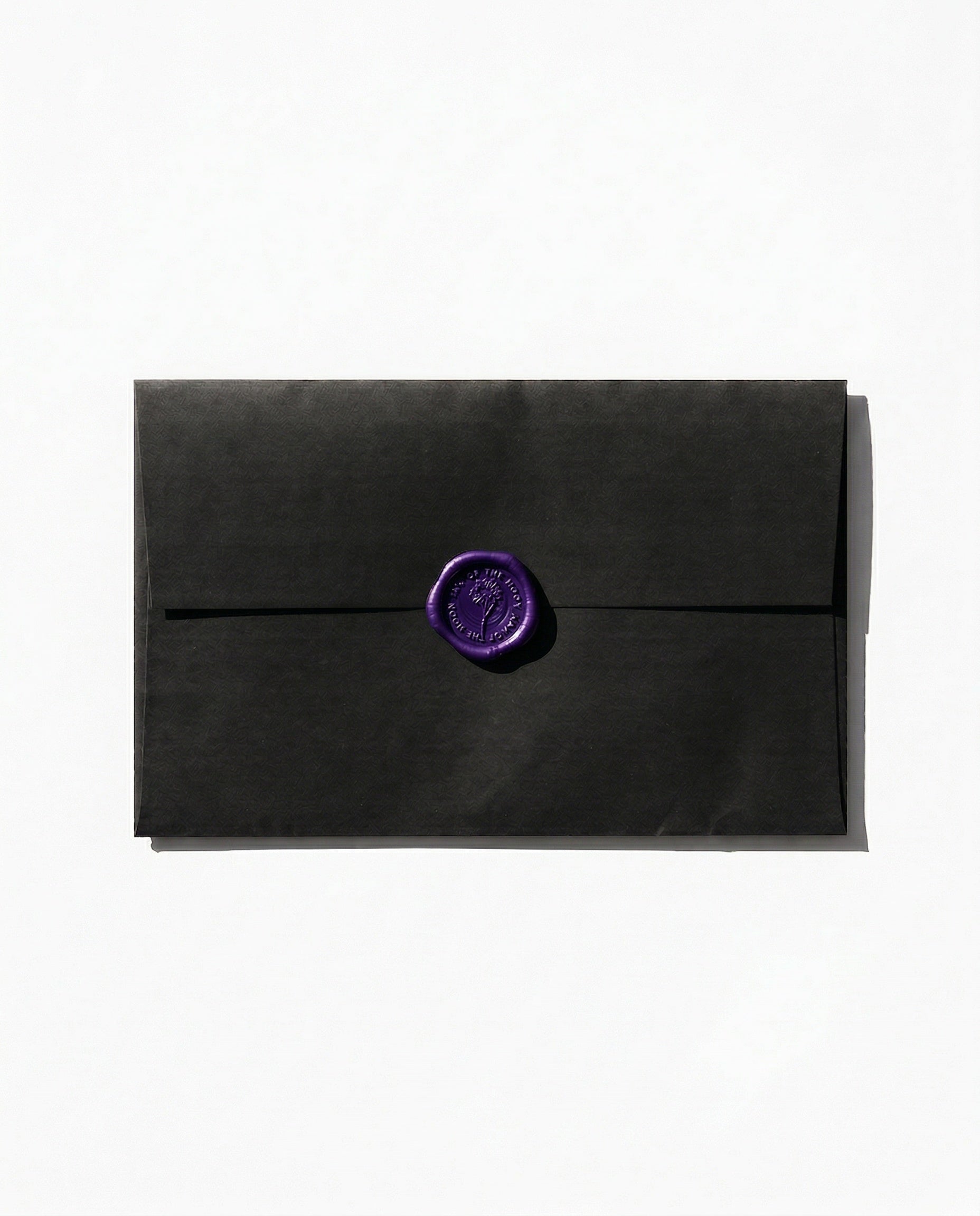 Black paper envelope with a dark purple wax seal against a white backdrop.