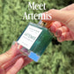 Close-up video featuring Artemis 30 mL body oil glass dropper bottle displayed against a dark evergreen background.